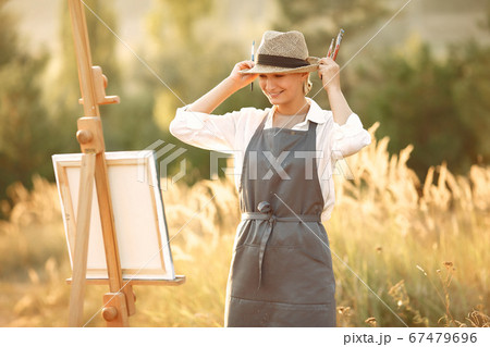 Woman in a apron painting in a field Woman in a apron painting in a field 67479696