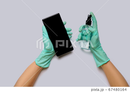 Female's hands in latex gloves wiping mobile phone with alcohol decontaminating agent top view over light grey background Female's hands in latex gloves wiping mobile phone with alcohol decontaminating agent top view over light grey background 67480164