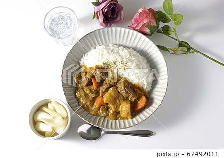 ジャガイモやニンジンがたくさん入った牛すじカレーとお冷やらっきょう そして薔薇の造花の写真素材