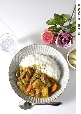 ジャガイモやニンジンがたくさん入った牛すじカレーとお冷やらっきょう、そして薔薇の造花 67492016