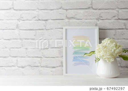 An abstract picture frame stands the will of a white brick wall. Green hydrangea in a vase in the Nordic style. An abstract picture frame stands the will of a white brick wall. Green hydrangea in a vase in the Nordic style. 67492297