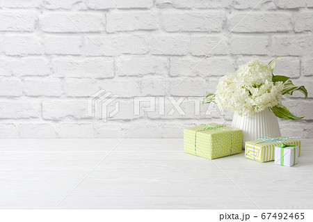 Little green gifts and a bouquet of white hydrangea in a vase. brick wall and white wooden table. Little green gifts and a bouquet of white hydrangea in a vase. brick wall and white wooden table. 67492465