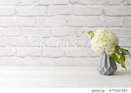 Green hydrangea in a gray vase in the Nordic style stands on a white wooden table. Background old brick. Bundle, copy space. Green hydrangea in a gray vase in the Nordic style stands on a white wooden table. Background old brick. Bundle, copy space. 67492485