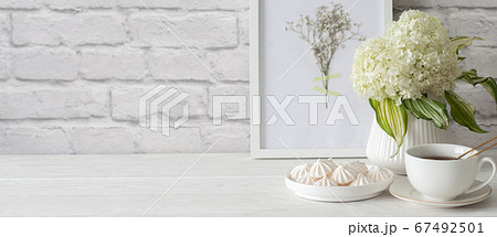 Tea in a cup with a golden strainer. Bizet on a plate. Frame with dried flowers. Aged white brick background. Green hydrangea in a vase in the Nordic style. 67492501