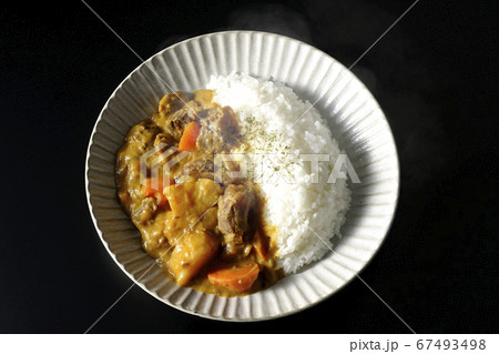 熱々で湯気が上がるジャガイモ、人参、牛すじ肉がたくさん入ったカレーライス（黒背景） 67493498