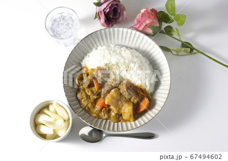 ジャガイモやニンジンがたくさん入った熱々の牛すじカレーとお冷やらっきょう、そして薔薇の造花 67494602