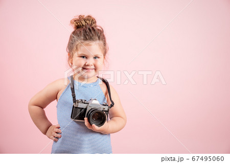 Little girl holding old vintage camera and smiling on pink background 67495060