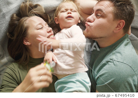 Top view of funny happy family in bed in the morning in casual clothes, young 30s parents 67495410