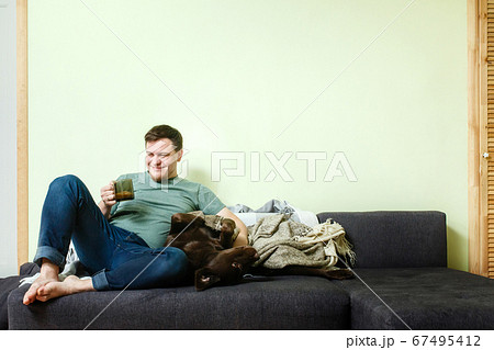 Happy handsome man sitting on the couch at home with pet dog labrador retriever Happy handsome man sitting on the couch at home with pet dog labrador retriever 67495412