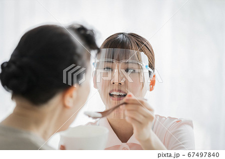 フェイスシールドをつけて食事介助を行う介護スタッフ 67497840