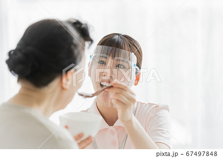 フェイスシールドをつけて食事介助を行う介護スタッフ 67497848