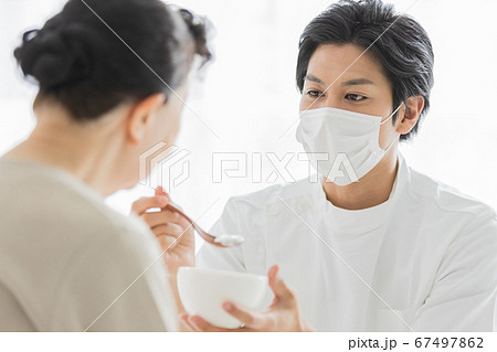 マスクをつけて食事介助を行う介護スタッフ 67497862