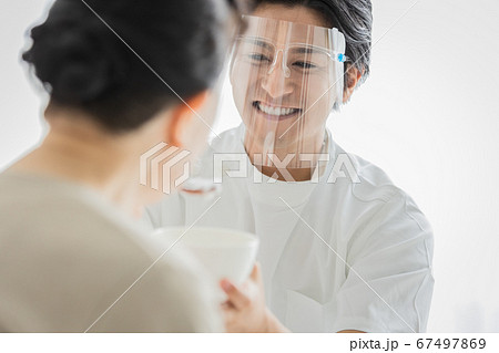 フェイスシールドをつけて食事介助を行う介護スタッフ 67497869