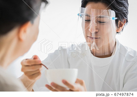 フェイスシールドをつけて食事介助を行う介護スタッフ 67497874