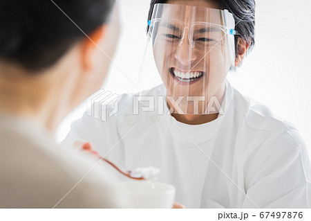 フェイスシールドをつけて食事介助を行う介護スタッフ 67497876