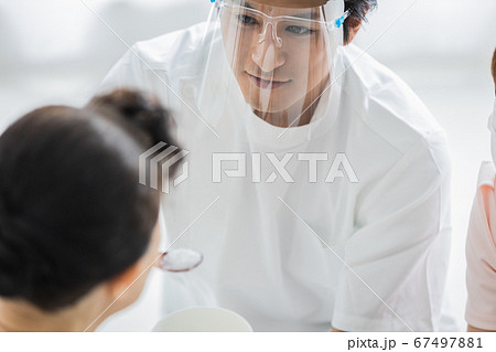 フェイスシールドをつけて食事介助を行う介護スタッフ 67497881