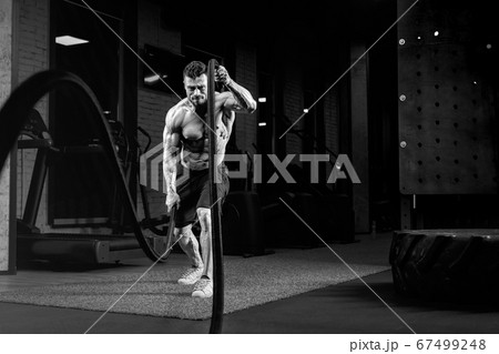 Monochrome portrait of shirtless man training with ropes. 67499248