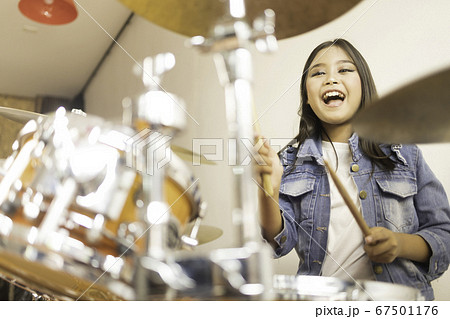 A cute Asian elementary school girl  laughing happily while playing a drum  67501176
