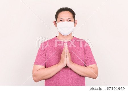 Portrait of Asian man wearing white fabric mask and showing Thai greeting (Wai gesture) Portrait of Asian man wearing white fabric mask and showing Thai greeting (Wai gesture) 67501969
