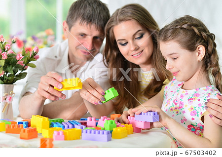 Girl with mother and father playing with colorful plastic blocks 67503402