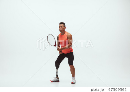 Athlete with disabilities or amputee isolated on white studio background. Professional male tennis player with leg prosthesis training and practicing in studio. 67509562