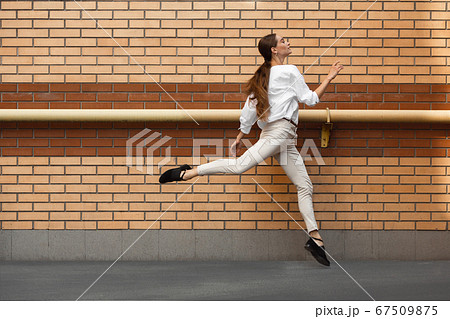 Jumping young woman in front of buildings, on the run in jump high 67509875