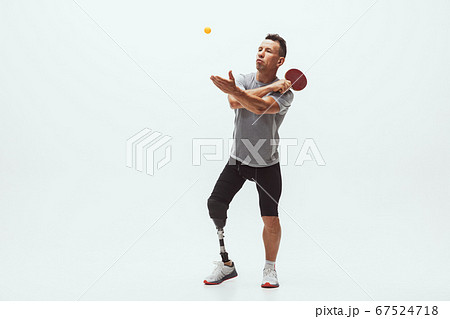 Athlete with disabilities or amputee isolated on white studio background. Professional male table tennis player with leg prosthesis training and practicing in studio. Athlete with disabilities or amputee isolated on white studio background. Professional male table tennis player with leg prosthesis training and practicing in studio. 67524718