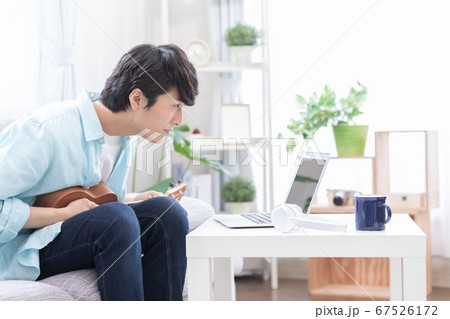 オンラインで楽器（ウクレレ）のレッスンを受ける若い男性 67526172