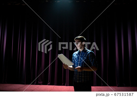 Stand up comedian on stage. Young man talks joke into microphone or sings songs. 67531587