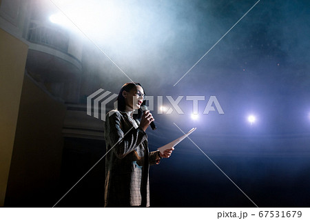 Expert perform on the stage address to modern crowd audience sitting and listening in large hall. Female entrepreneur communicating with a listener at workshop convention for young businesspersons 67531679