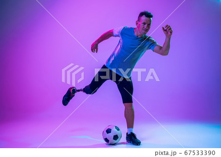 Athlete with disabilities or amputee isolated on gradient studio background. Professional male football player with leg prosthesis training and practicing in studio. 67533390