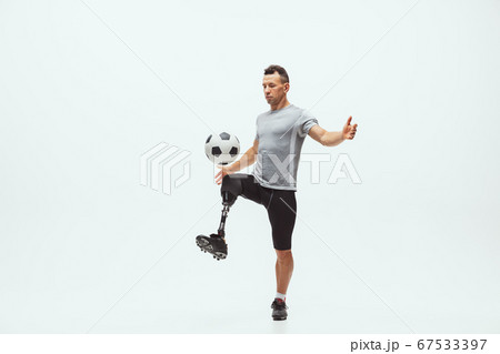 Athlete with disabilities or amputee isolated on white studio background. Professional male football player with leg prosthesis training and practicing in studio. 67533397