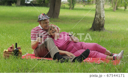 Family weekend picnic in park. Active senior old caucasian couple sit on blanket and drink wine Family weekend picnic in park. Active senior old caucasian couple sit on blanket and drink wine 67544171