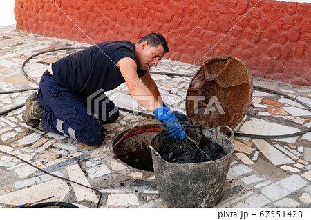 Worker cleans the drains hatch and removes dirt and debris from the sewer. Plumber cleans the sewer Worker cleans the drains hatch and removes dirt and debris from the sewer. Plumber cleans the sewer 67551423