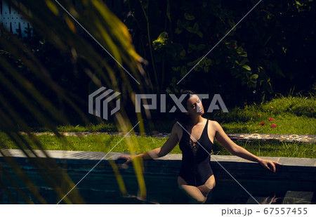 Young beautiful woman in black bikini in the pool during hot sunny summer day. Tropical vacation 67557455