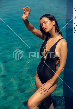 Young beautiful woman in black bikini in the pool during hot sunny summer day. Tropical vacation 67557456