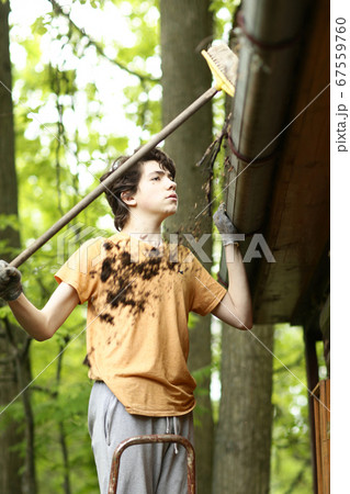 closeup photo of teenager boy cleaning roof from old leafs closeup photo of teenager boy cleaning roof from old leafs 67559760