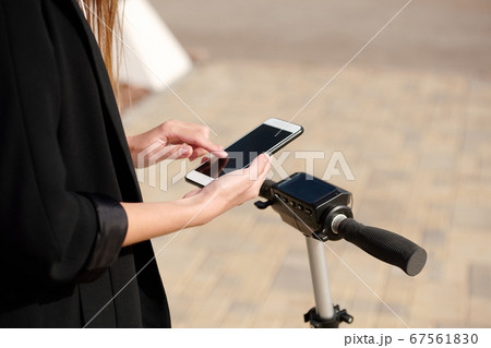 Hands of young female scrolling in smartphone while standing on electric scooter Hands of young female scrolling in smartphone while standing on electric scooter 67561830