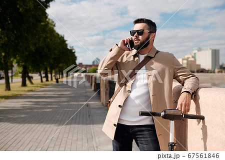 Young elegant agent with electric scooter talking on mobile phone outdoors 67561846