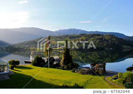 ノルウェー　ハダンゲルフィヨルド、ウルヴィク地区、さわやかな朝の山と水面と空と遊覧船のある風景を望む 67562049