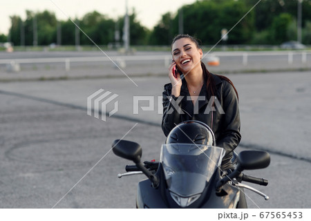 Portrait of a serious biker waiting during a phone call to insurance on a motorbike on the street 67565453