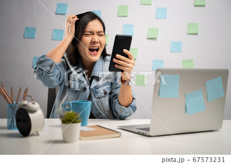 Asian woman angry looking at smart phone reading Asian woman angry looking at smart phone reading 67573231