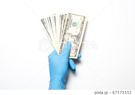 The collapse of the economy due to the coronavirus. Male hand on a white background in medical gloves holds dollars. The collapse of the economy due to the coronavirus. Male hand on a white background in medical gloves holds dollars. 67575552