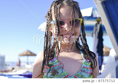 Little girl in a swimsuit on the beach plays, smiles. Child 7 years old on the equipped beach of 67575712