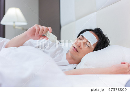 体温計で熱を測る若い男性 体温計で熱を測る若い男性 67578309