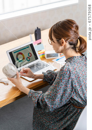 テレワーク中に卓上扇風機の風量を調整する若い女性 67579368