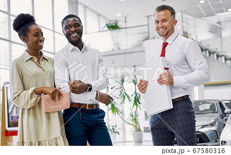 friendly salesman and beautiful couple in car showroom friendly salesman and beautiful couple in car showroom 67580316