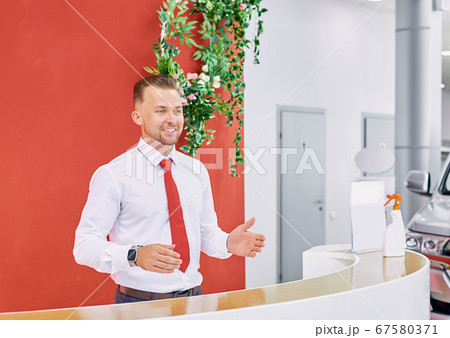 smiling sales expert welcoming customers in car showroom 67580371