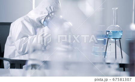 Scientist in PPE suite doing some research and looking through a microscope in laboratory 67581307