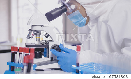 Scientist in PPE suite doing some research and looking through a microscope in laboratory 67581308